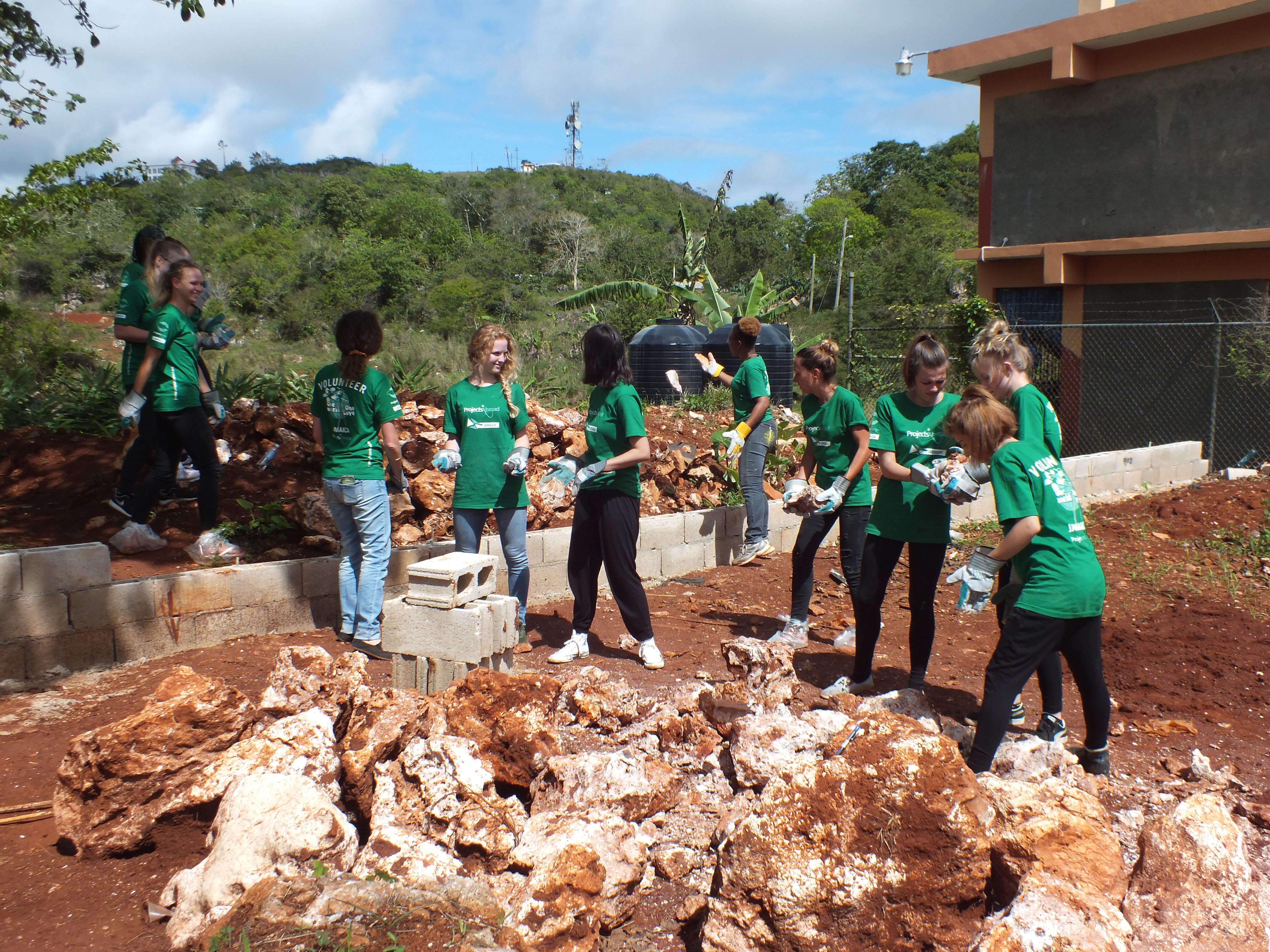 Volunteers team up to clear ground and build a playground at a disadvantaged school in Jamaica. A group doing building volunteer work in Jamaica help clear ground at a school to construct a playground.